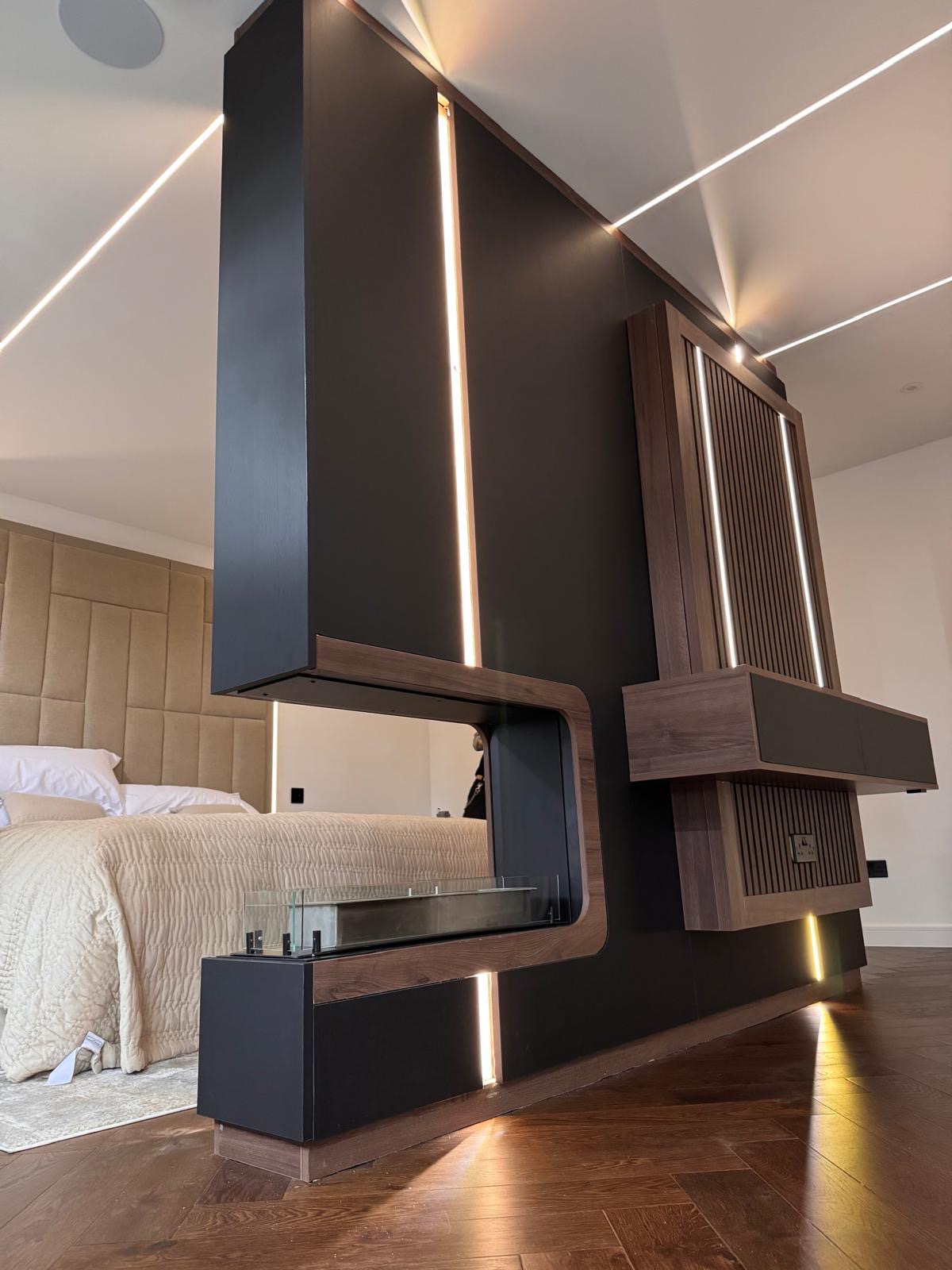 Bespoke bedroom media wall in matt black and walnut with a glass-fronted linear fire, floating drawers and recessed LED lighting