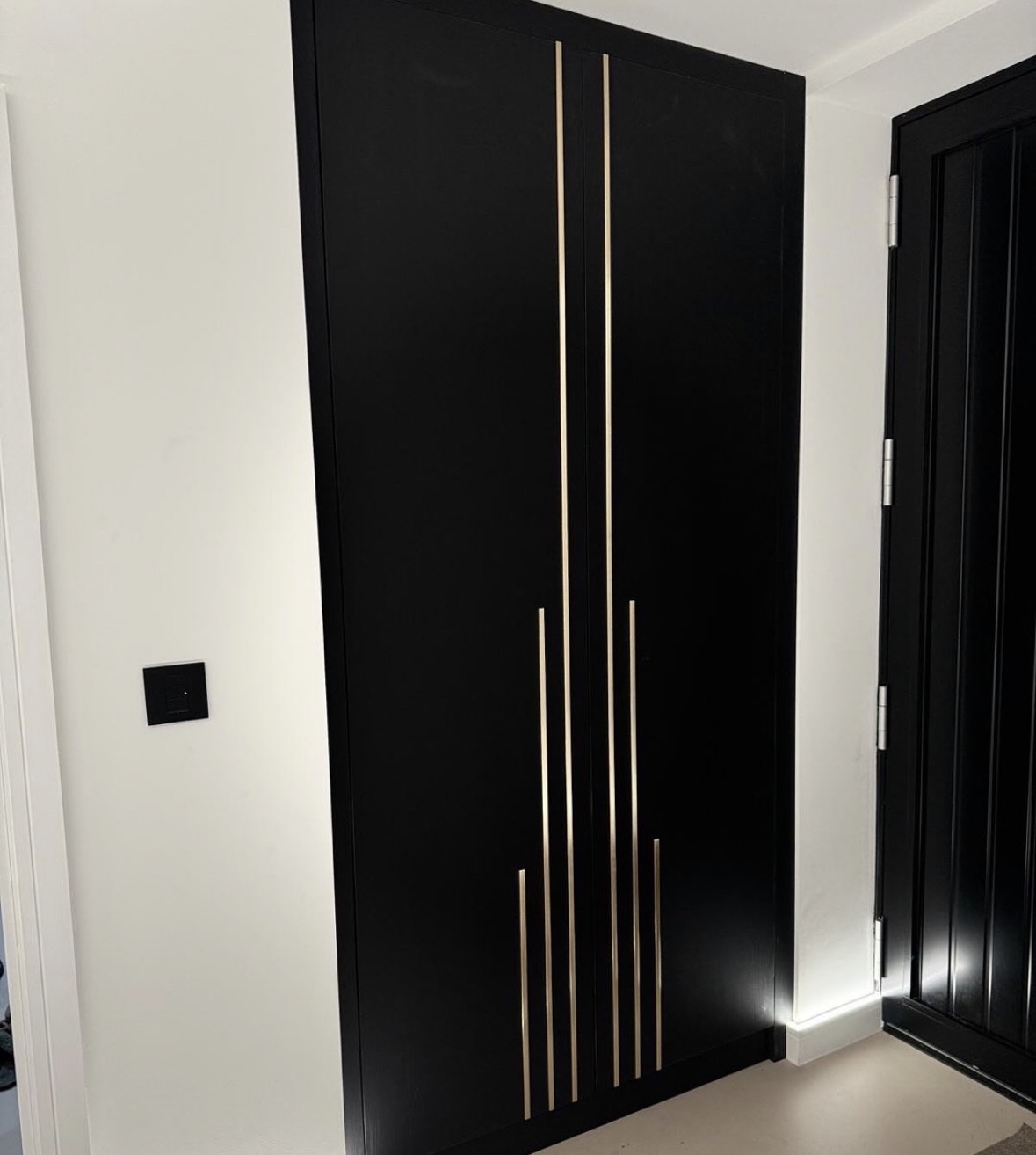 Floor-to-ceiling fitted wardrobe in matt black with vertical brass inlay detailing
