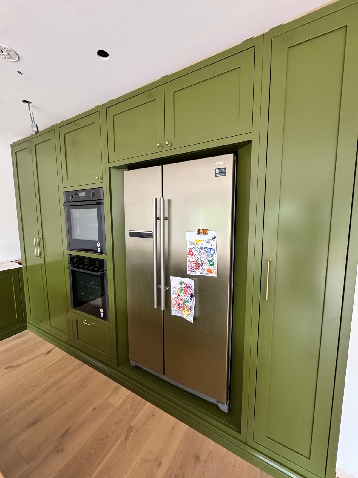 Hand-painted green shaker kitchen cabinetry housing an American-style fridge freezer and built-in double ovens with brass handles
