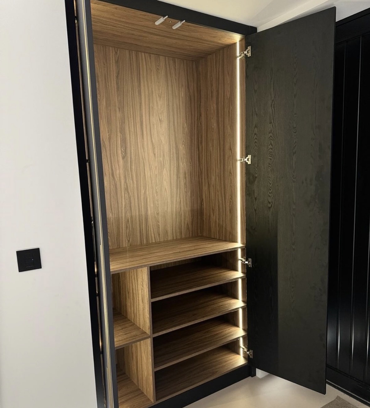 Interior of a fitted wardrobe with walnut shelving, adjustable shoe racks and integrated LED lighting