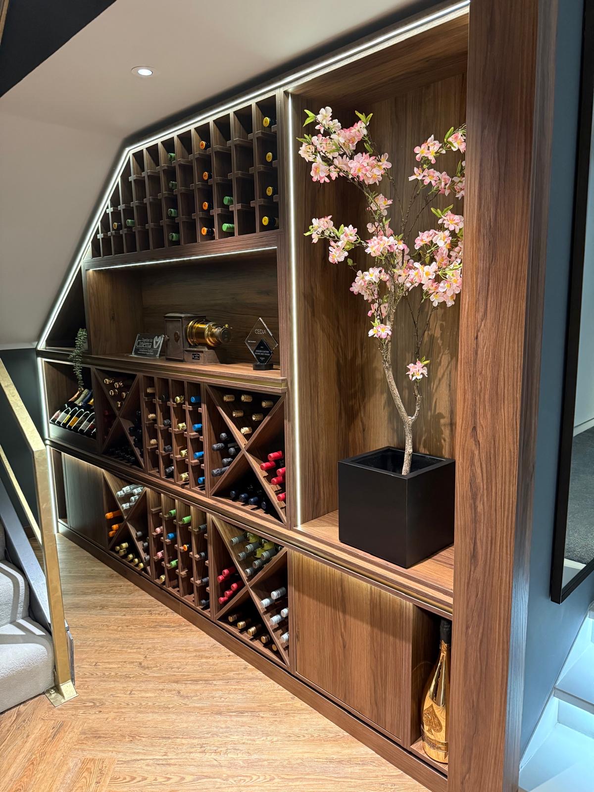 Bespoke wine wall in walnut with individual bottle racking, display shelving and integrated LED lighting shaped to a sloping ceiling