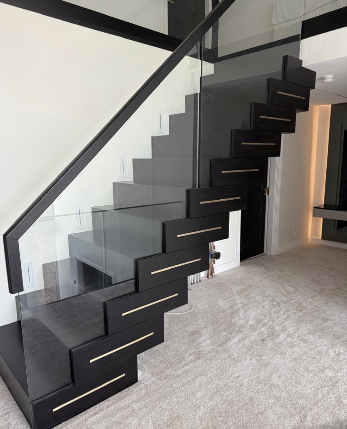 Bespoke black stained oak cantilevered staircase with inset brass tread strips and a frameless glass balustrade with timber handrail