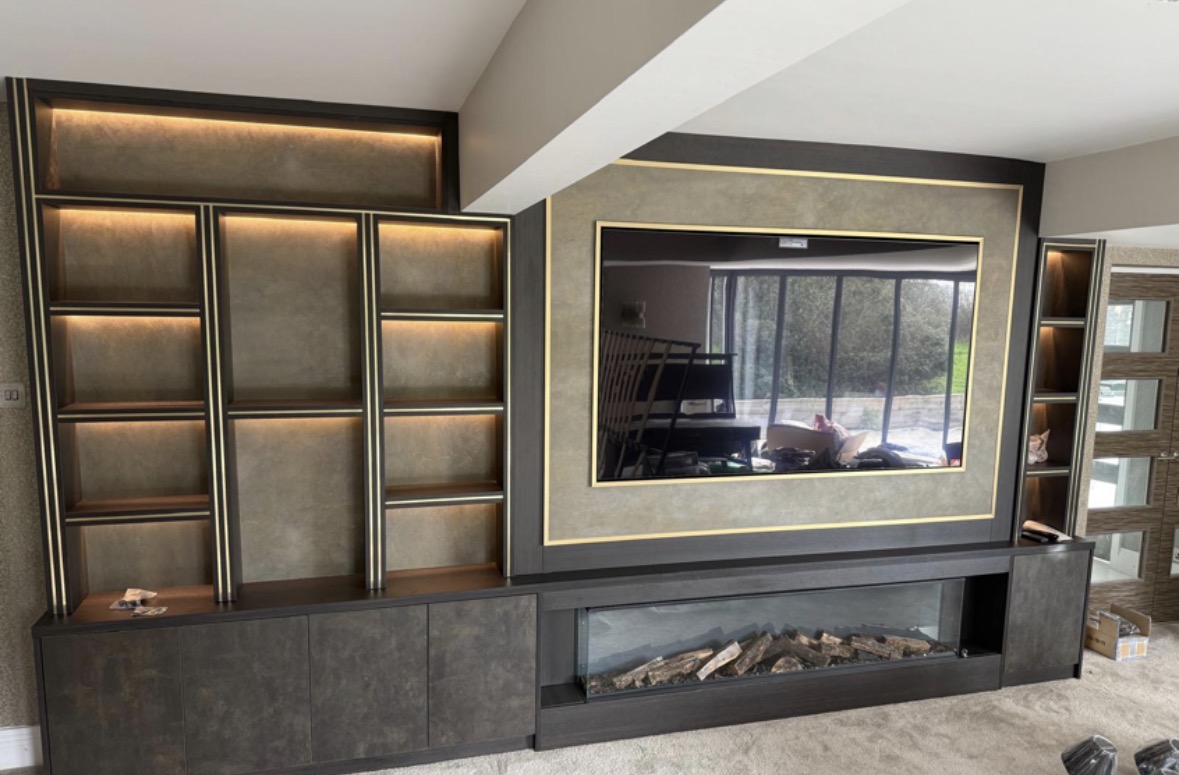 Bespoke media wall in dark oak and bronze with a gold-framed television panel, LED-lit display shelving and a long inset log-effect fire