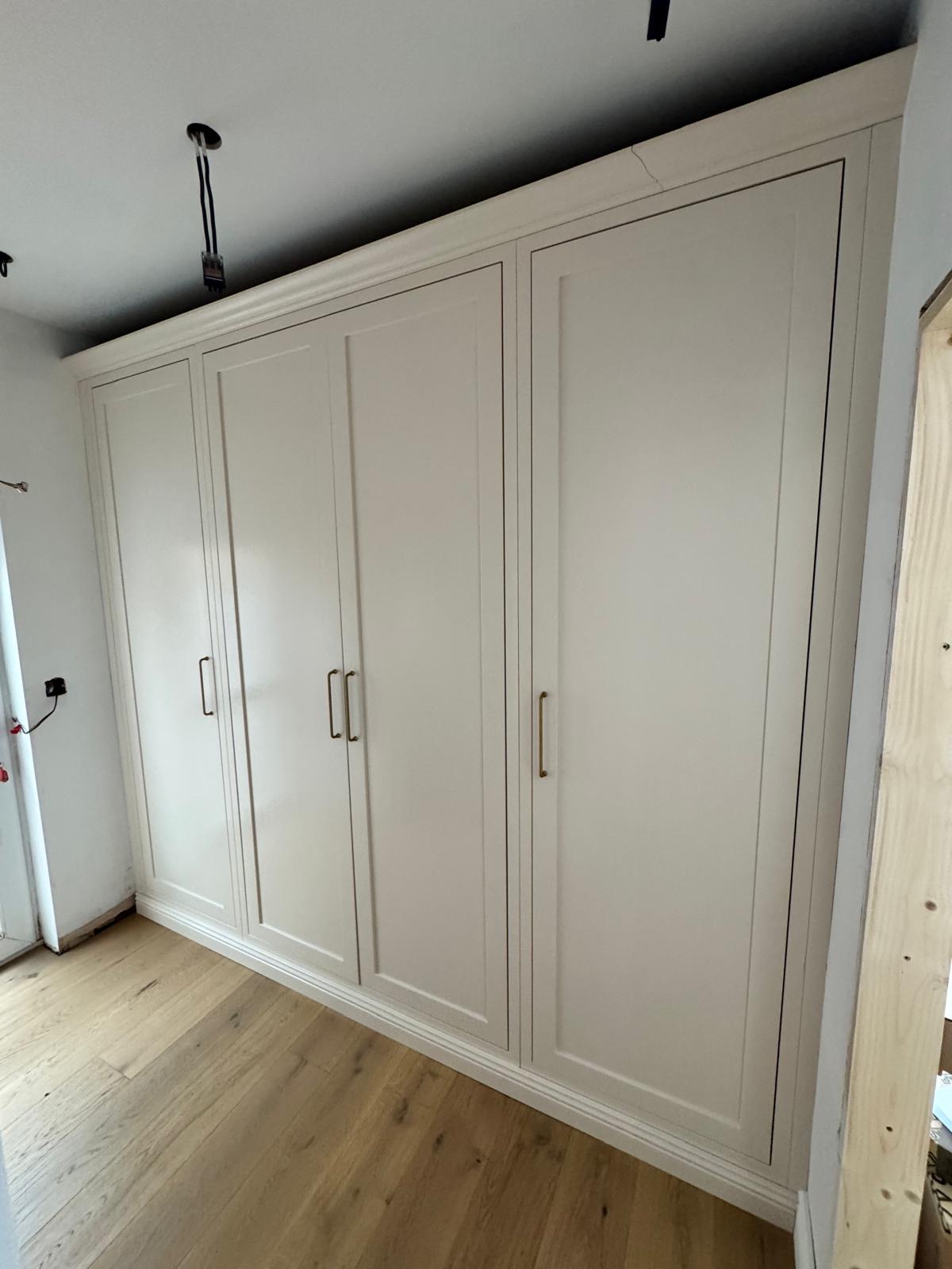 Run of floor-to-ceiling fitted wardrobes in cream shaker style with slim brass bar handles and a stepped cornice