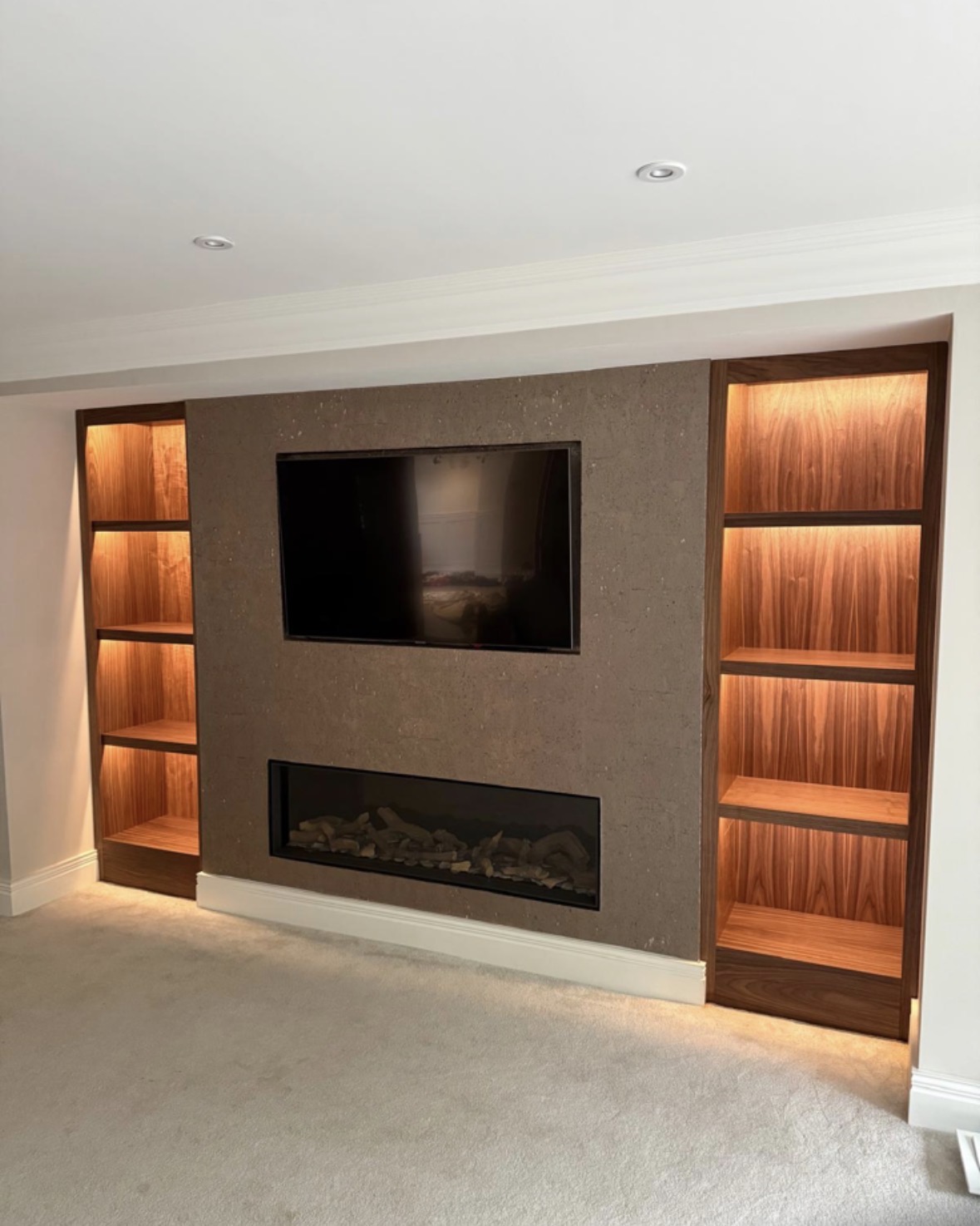 Bespoke media wall with stone-clad centre panel, recessed television, inset linear fire and LED-lit walnut bookcases either side