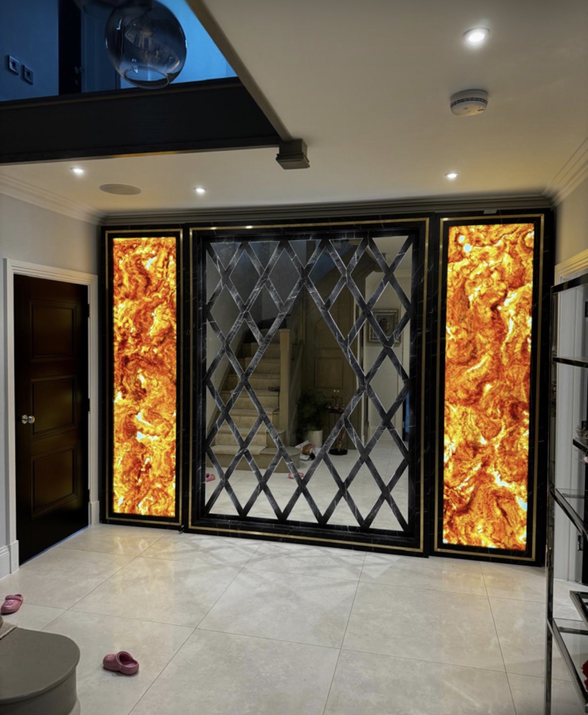 Bespoke hallway feature wall with backlit amber onyx panels, brass trims and a black marble diamond-lattice antique mirror centre panel